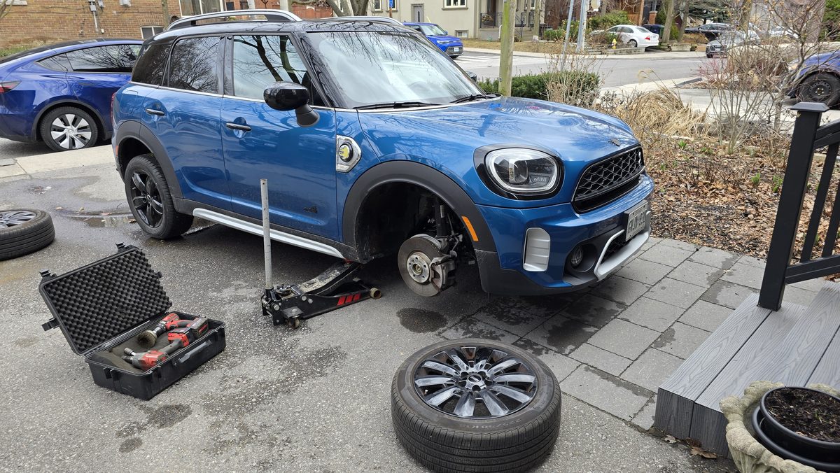 Blue Mini Countryman electric with its front wheel removed and the tool case out during a driveway tire service