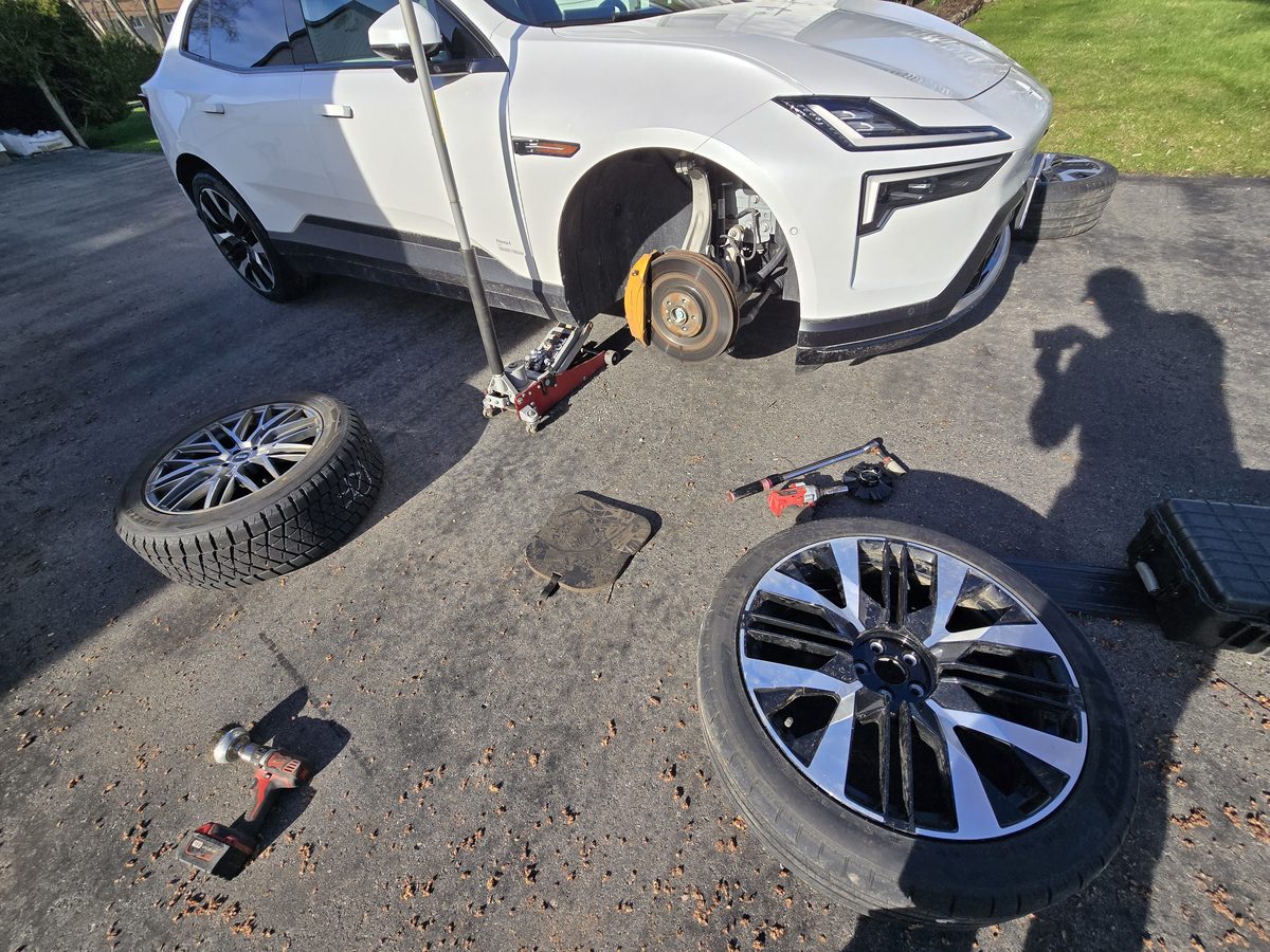 White Polestar with its front wheel removed on a jack during a driveway tire change