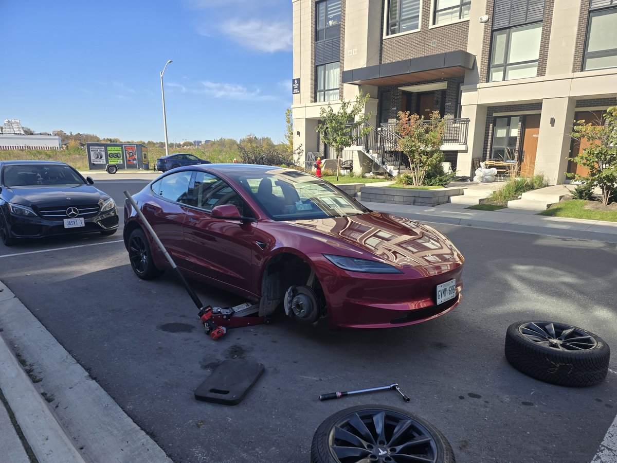 Red Tesla Model 3 with its wheel removed during a driveway tire service, Sparky X trailer behind